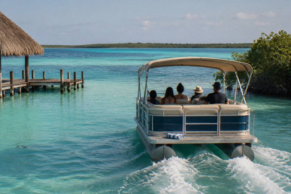 Pontoon boat with passengers crossing open turquoise water in Bacalar Lagoon