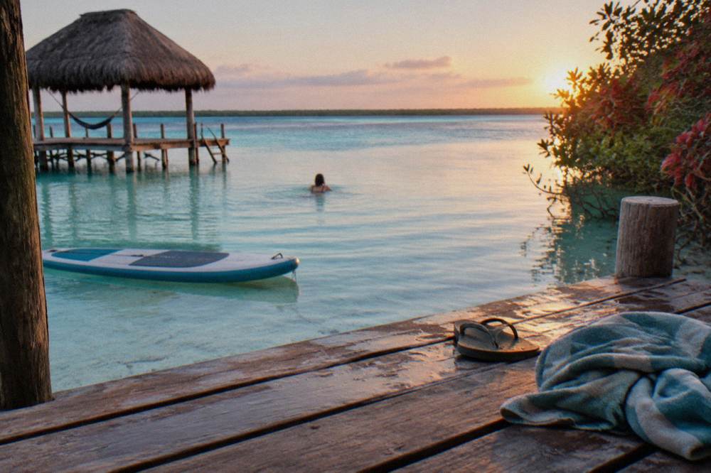 Swimmer in clear shallow water beside a moored paddleboard at sunrise