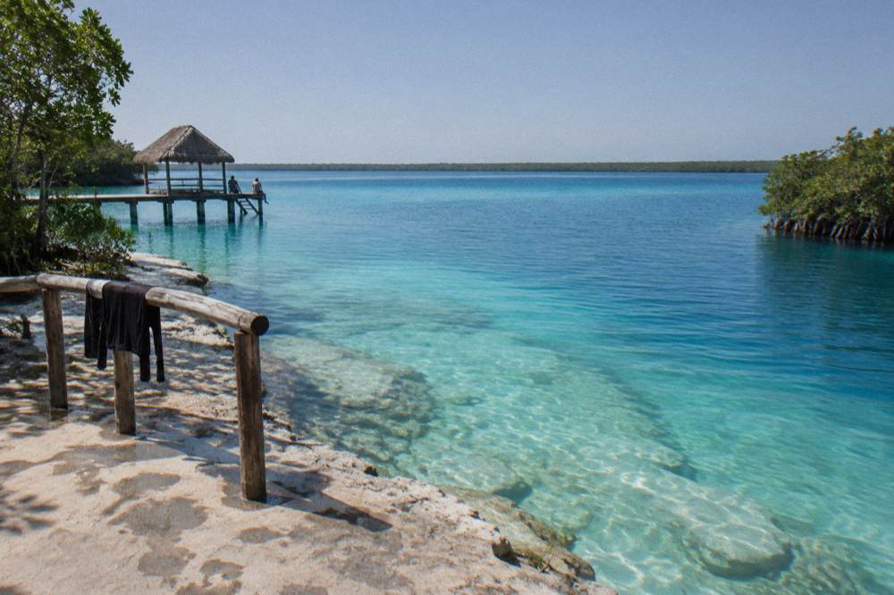 Calm turquoise lagoon water meeting a band of deeper blue under a clear morning sky