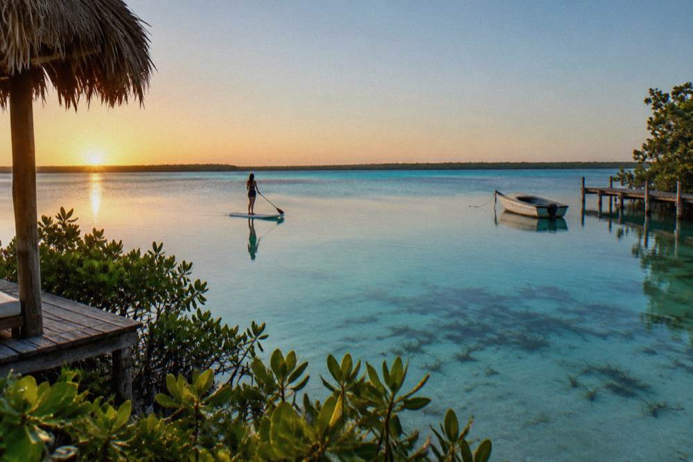 Paddleboarder gliding across mirror-flat turquoise water at sunrise