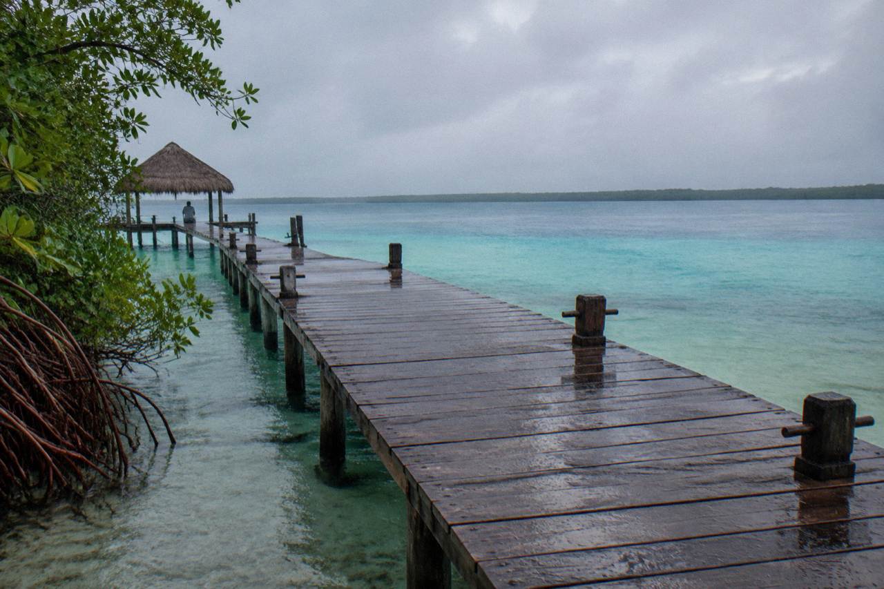Wooden dock extending over calm turquoise water of Bacalar Lagoon at dawn