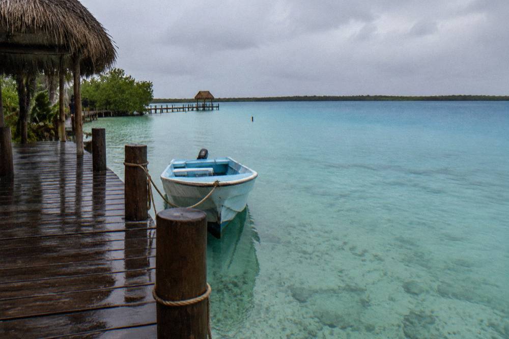 Small boat anchored in shallow clear water beside a wooden dock