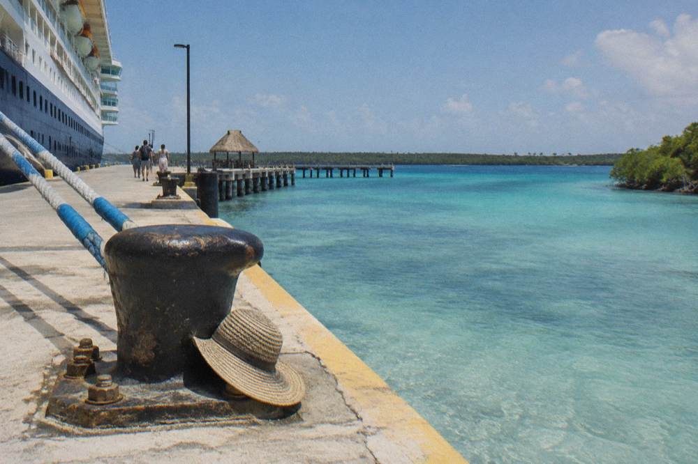 Cruise ship docked at a long pier beside a calm Caribbean shoreline