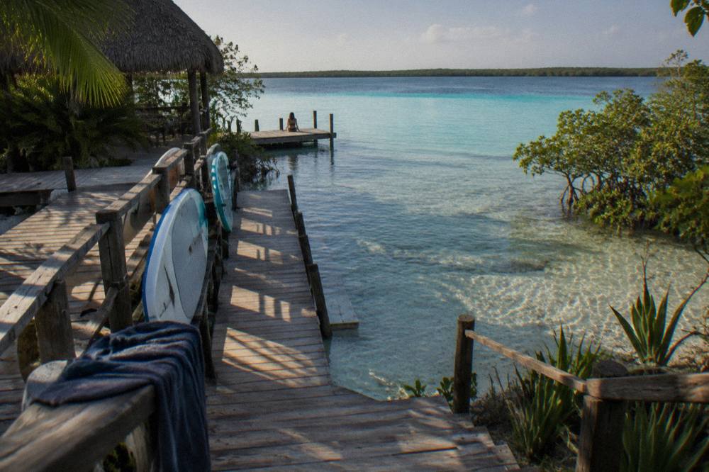 Row of paddleboards resting on a wooden dock above clear shallow lagoon water