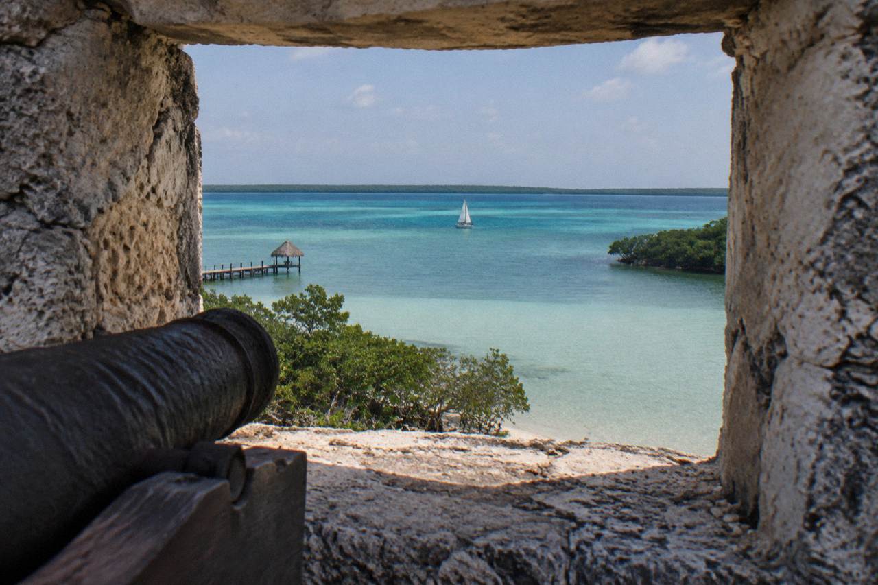 Sailboat crossing calm turquoise water on Bacalar lagoon under a pale morning sky