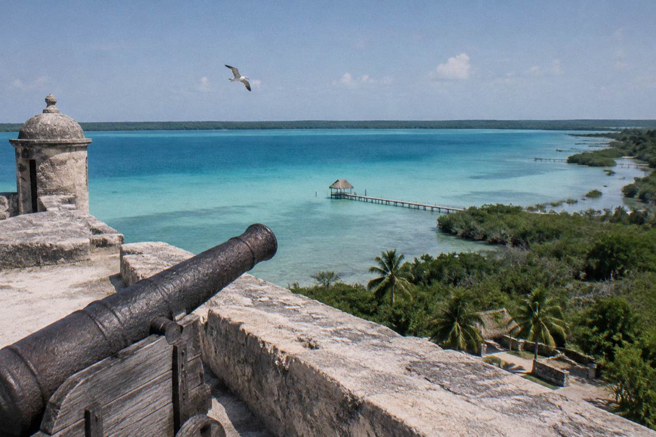 Wide view across Bacalar Lagoon with bands of blue and turquoise water under a clear sky