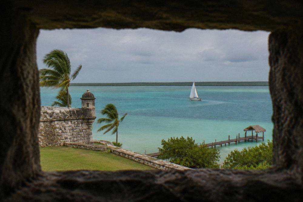 Sailboat crossing calm turquoise water on Bacalar Lagoon in morning light