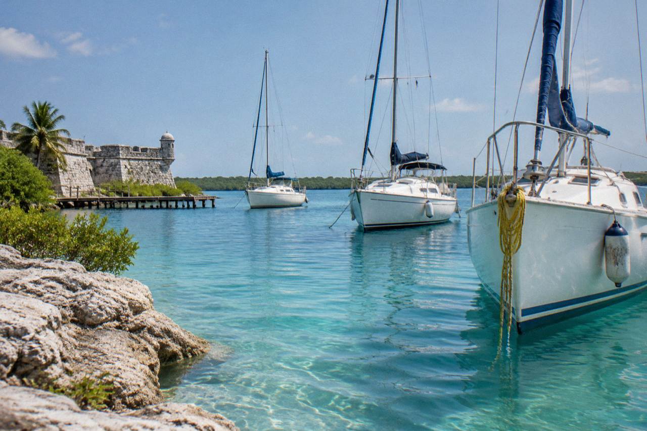 Turquoise water of Bacalar Lagoon under a bright sky with sailboats at anchor