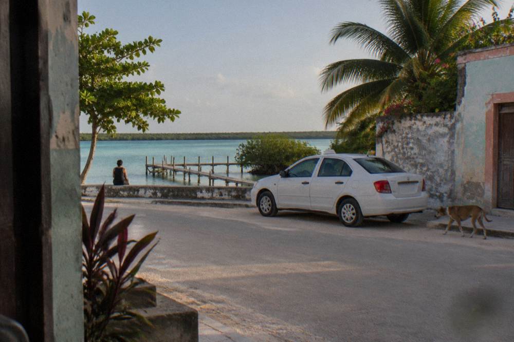 A quiet street in a small Mexican lagoon town with colorful low buildings and a parked taxi in late afternoon light