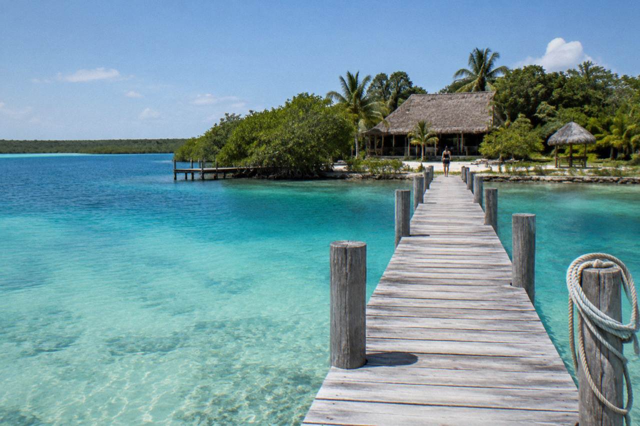 Calm turquoise water of a freshwater lagoon under a bright morning sky, with a wooden pier reaching into the shallows