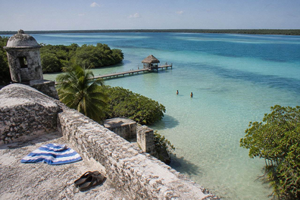 Clear turquoise water of Bacalar Lagoon under a bright morning sky, gentle ripples across the shallows