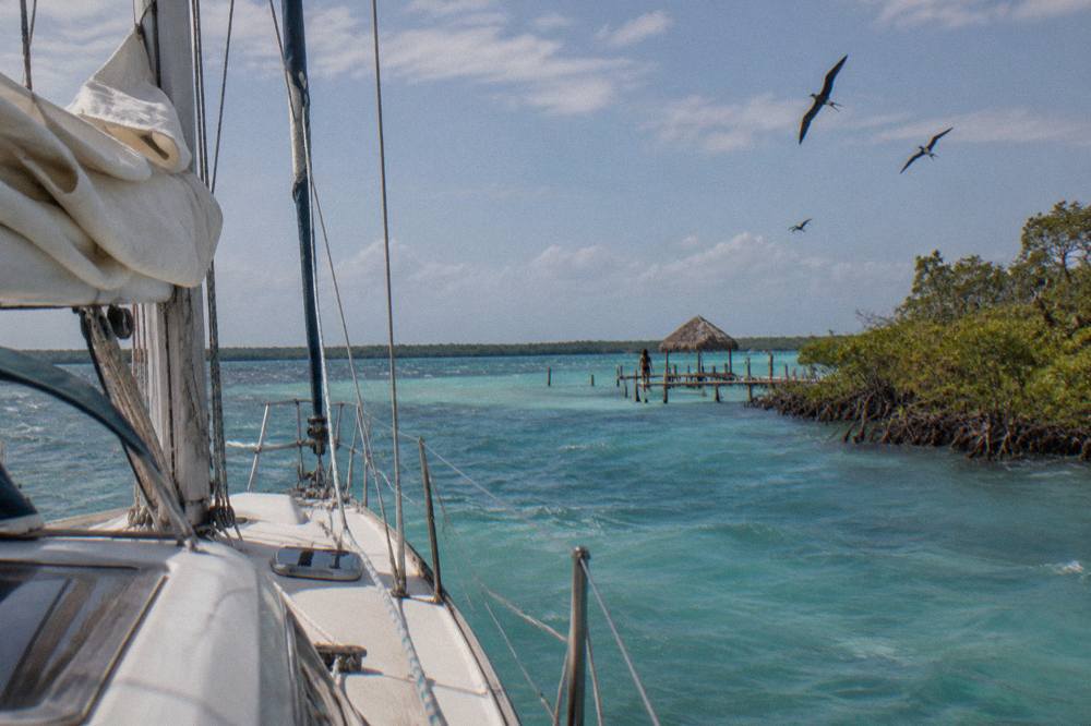 Sailboat on calm turquoise water in Bacalar Lagoon with mangrove shoreline