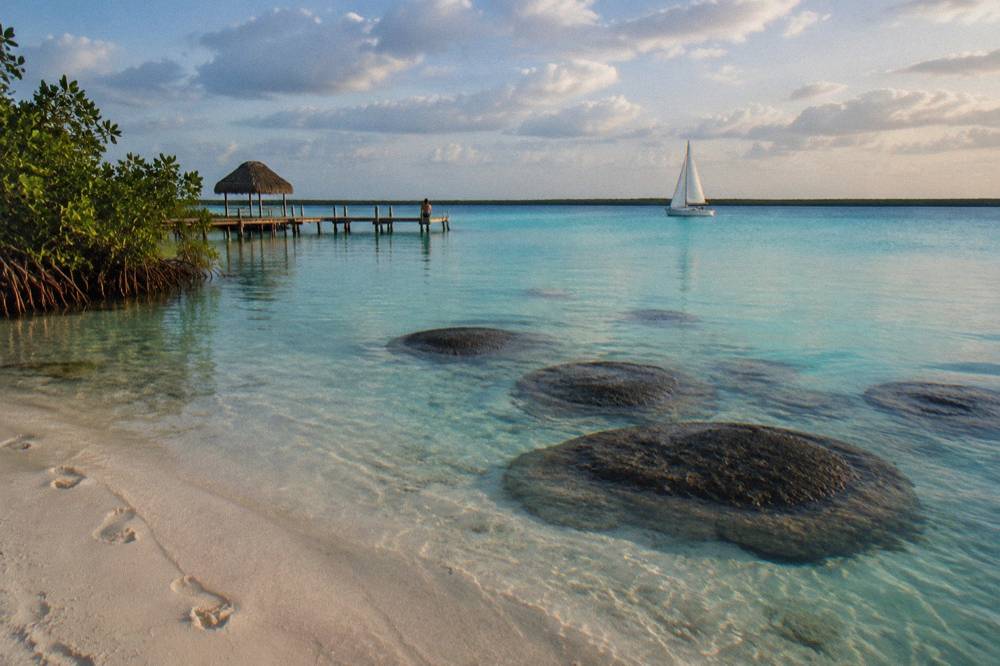 A sailboat passing at a distance above submerged dark microbialite domes in turquoise water