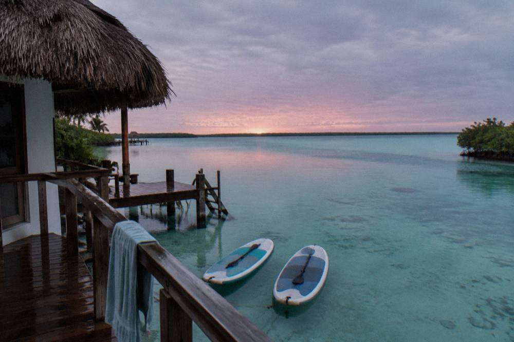 Paddleboards resting on still lagoon water at dawn with soft pink light over the horizon