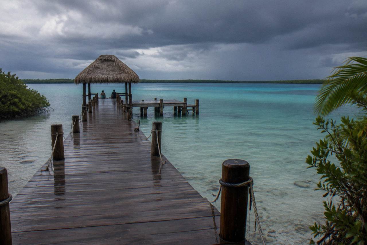 Rain clouds over the blue water of Bacalar lagoon with a wooden pier in the foreground