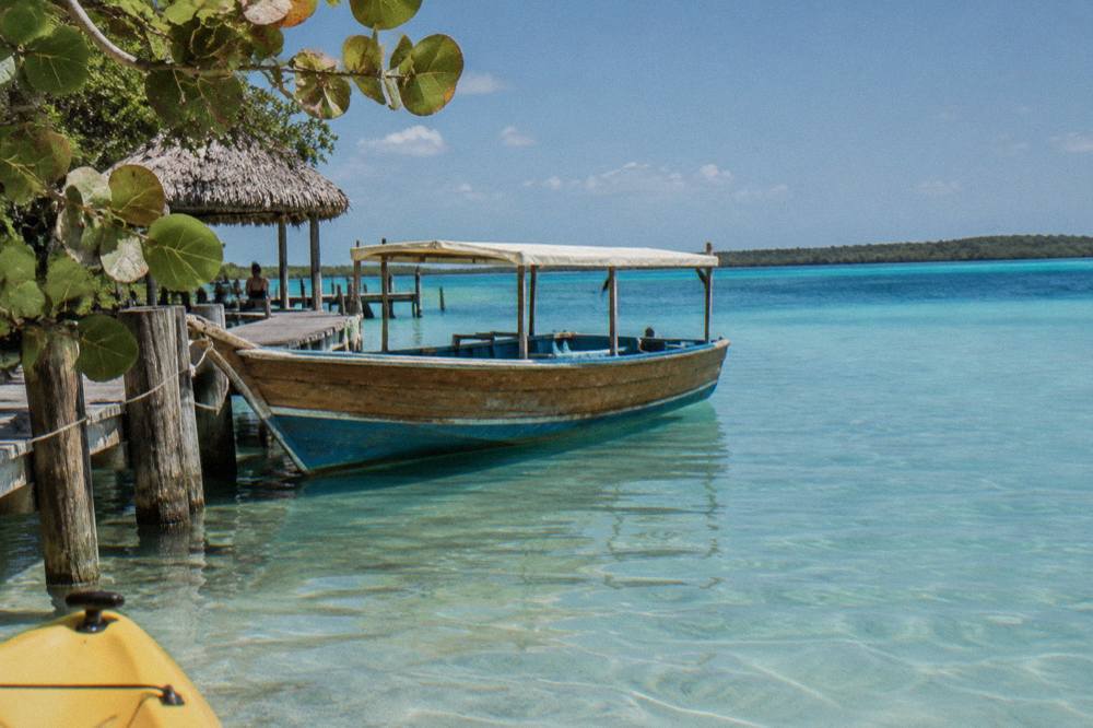 A wooden motor launch moored at a pier on Bacalar Lagoon with clear shallow water below