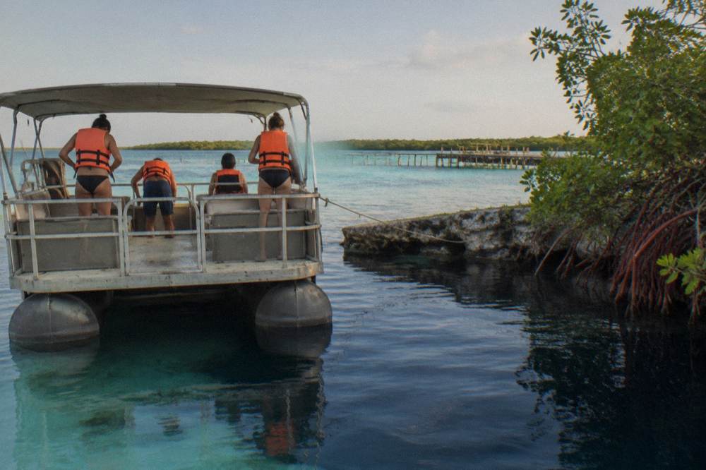 A pontoon boat at anchor in shallow turquoise water with passengers preparing to swim