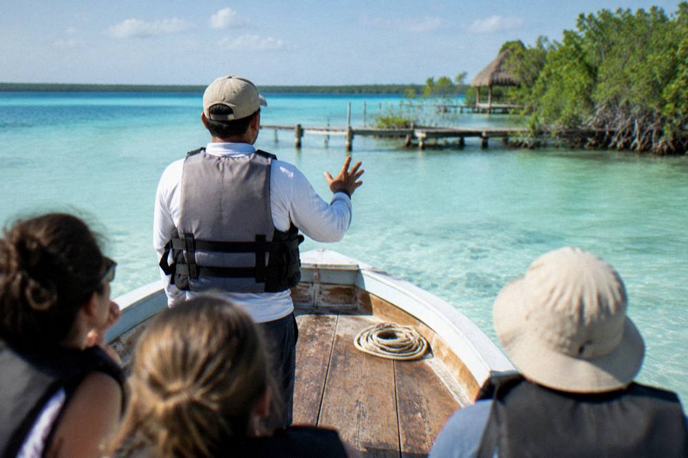A tour captain in a life jacket briefing passengers on the deck of a boat on Bacalar Lagoon