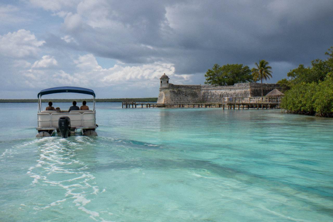 A pontoon boat crossing calm turquoise water on Bacalar Lagoon under a morning sky