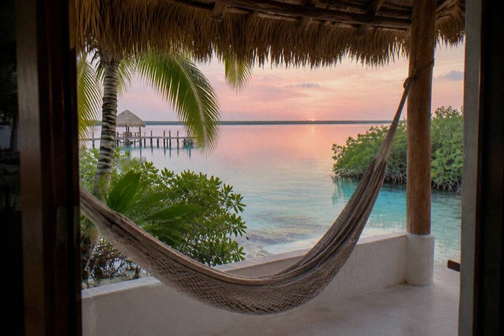 Small waterfront guesthouse with a hammock terrace overlooking the still lagoon at dawn