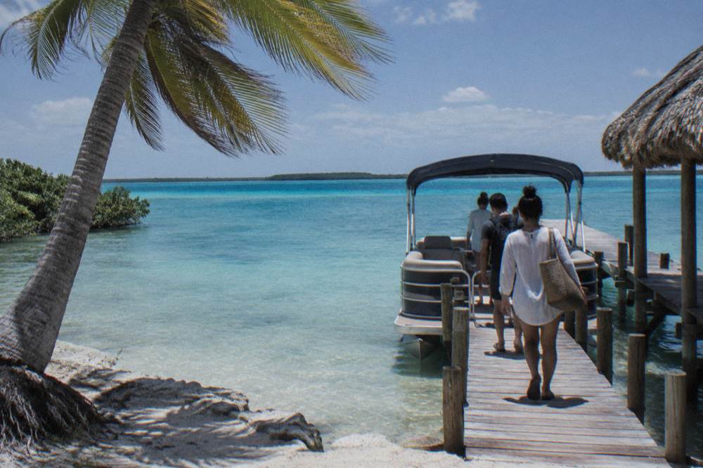 Small group of travelers boarding a pontoon boat at a wooden pier on turquoise lagoon water