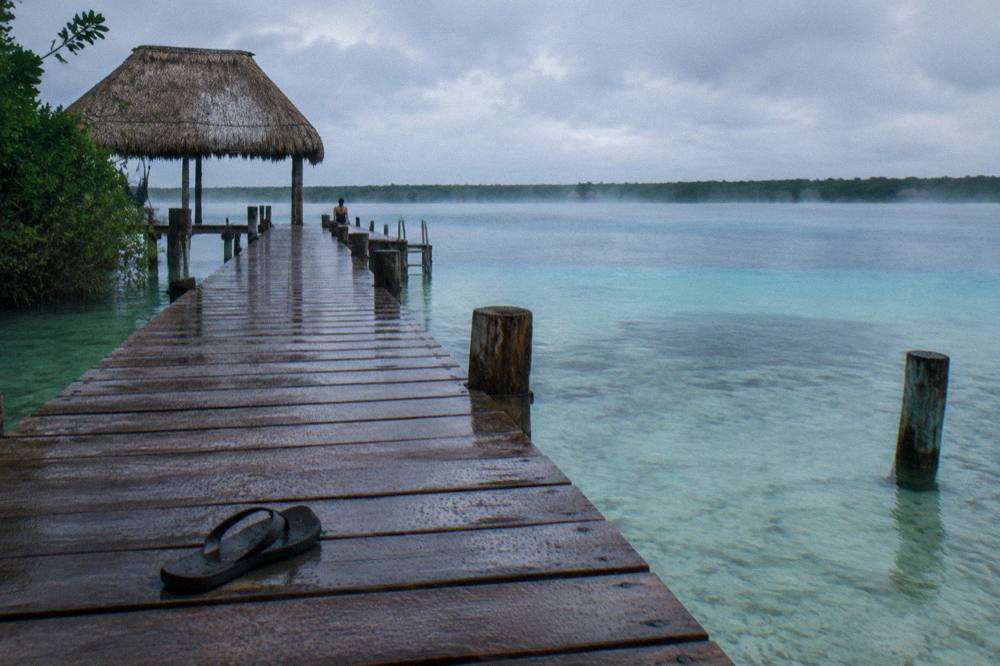 Long wooden dock reaching over clear shallow water toward distant tree-lined shoreline