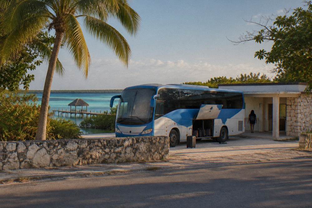 Blue and white ADO bus parked at a small station in warm afternoon light
