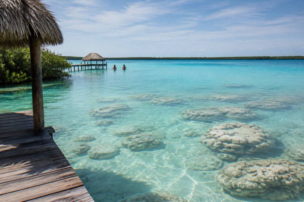 A floating picnic spread of fruit, toast and coffee served on a paddle board in shallow clear water