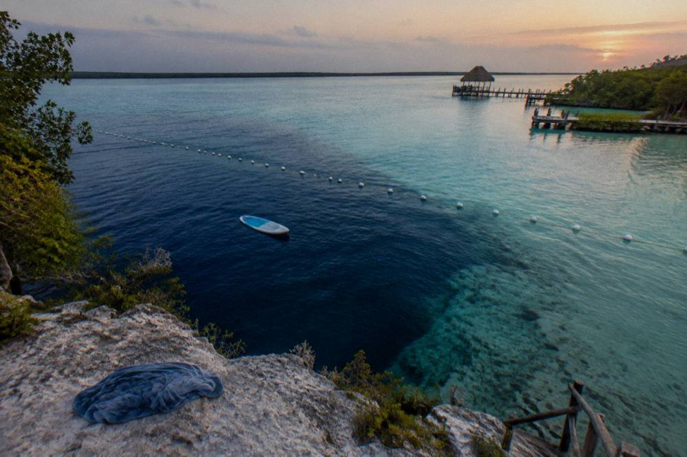A paddle board floating above dark deep water where a round cenote pool meets turquoise shallows