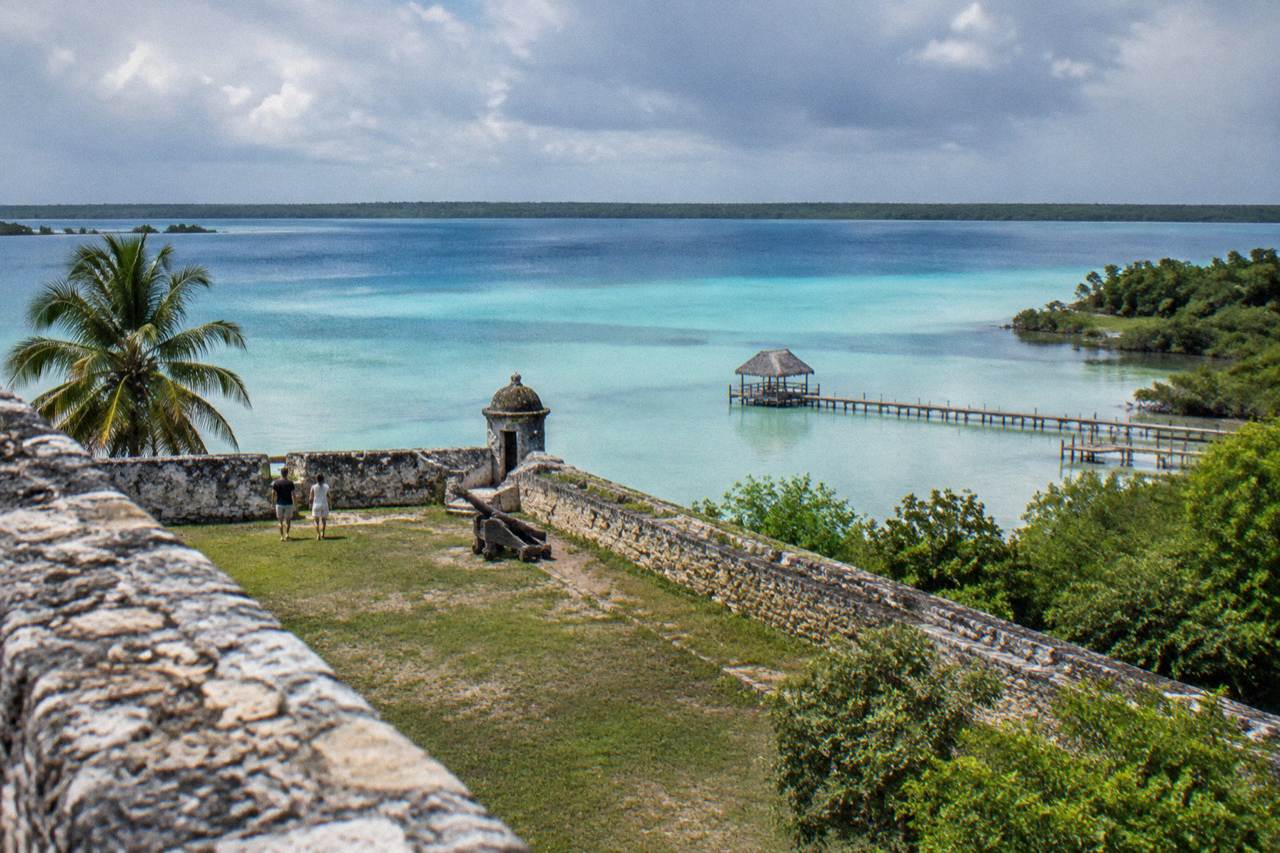 Wide view across Bacalar Lagoon with bands of turquoise and deep blue water under a morning sky