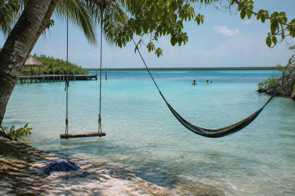 Wooden swings and a hammock suspended over clear shallow water at a Bacalar lagoon club