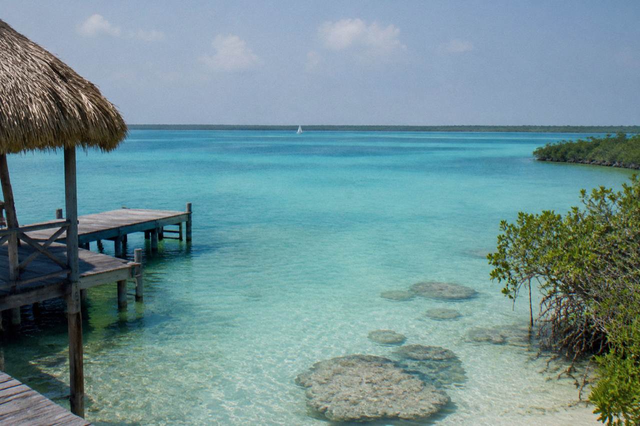Turquoise water of Bacalar Lagoon with a small sailboat on the horizon under a clear sky