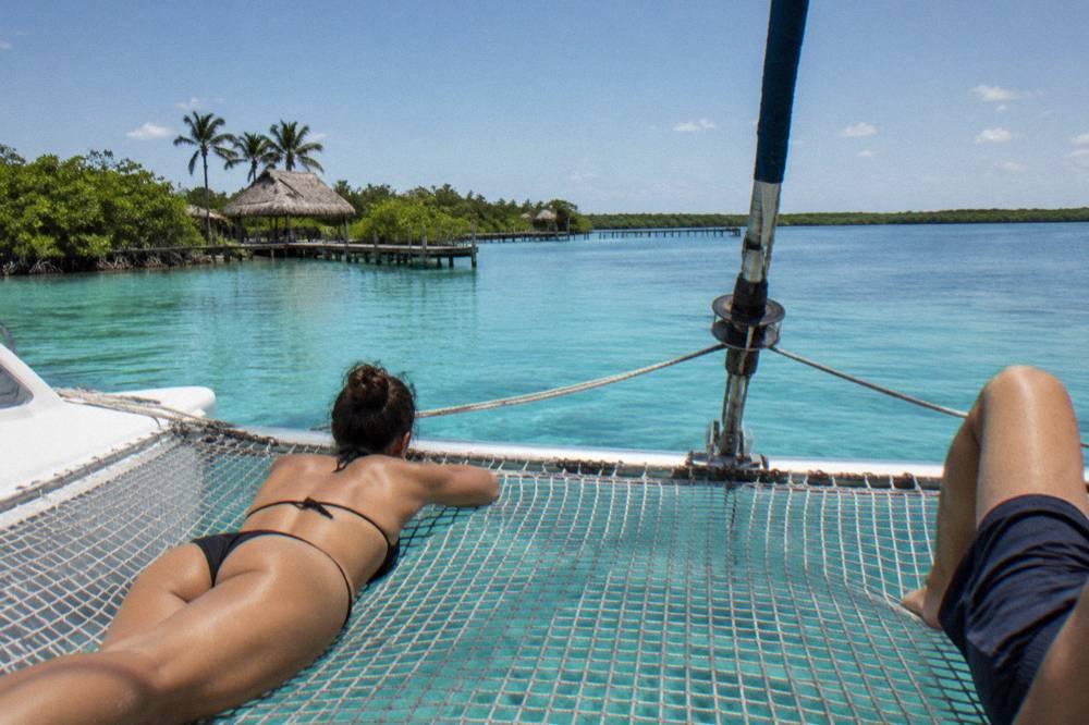 Passengers relaxing on the bow netting of a sailing catamaran on bright turquoise water