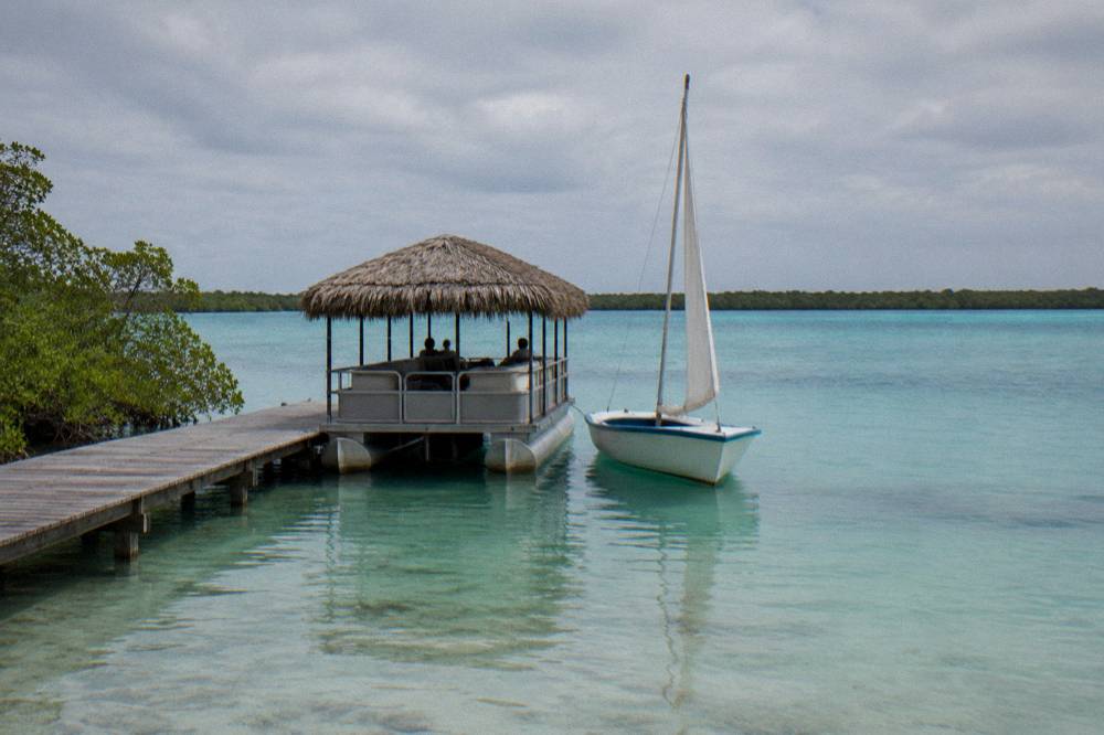 A pontoon boat and a sailboat anchored side by side in shallow turquoise water