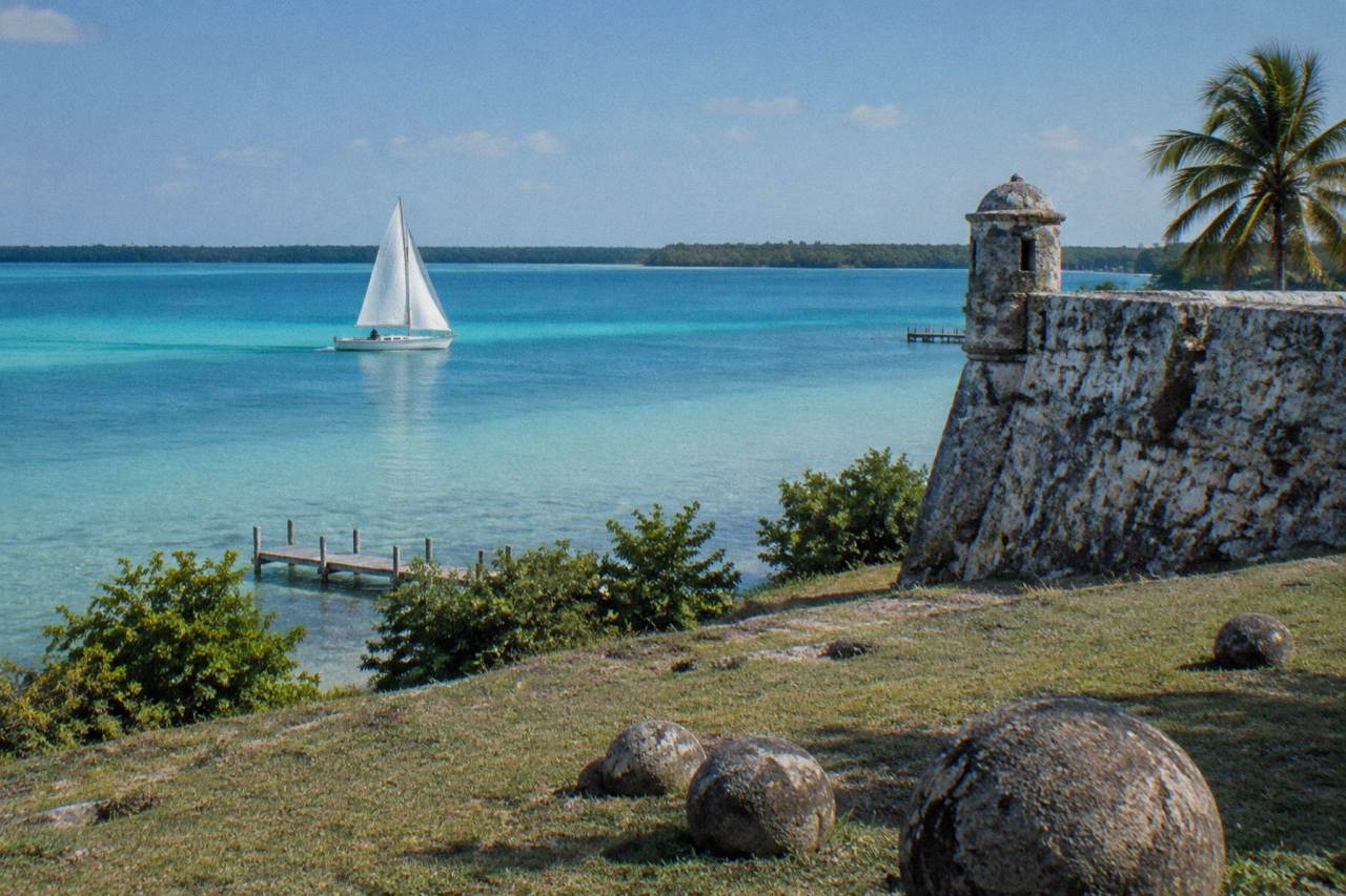 A sailboat crossing calm turquoise water on Bacalar Lagoon under a clear sky
