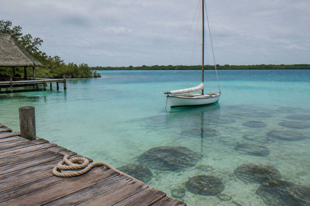 Sailboat passing slowly over shallow lagoon water with dark formations below the surface