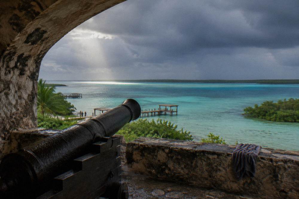 Dark rain clouds over Bacalar Lagoon with sunlight breaking on turquoise water