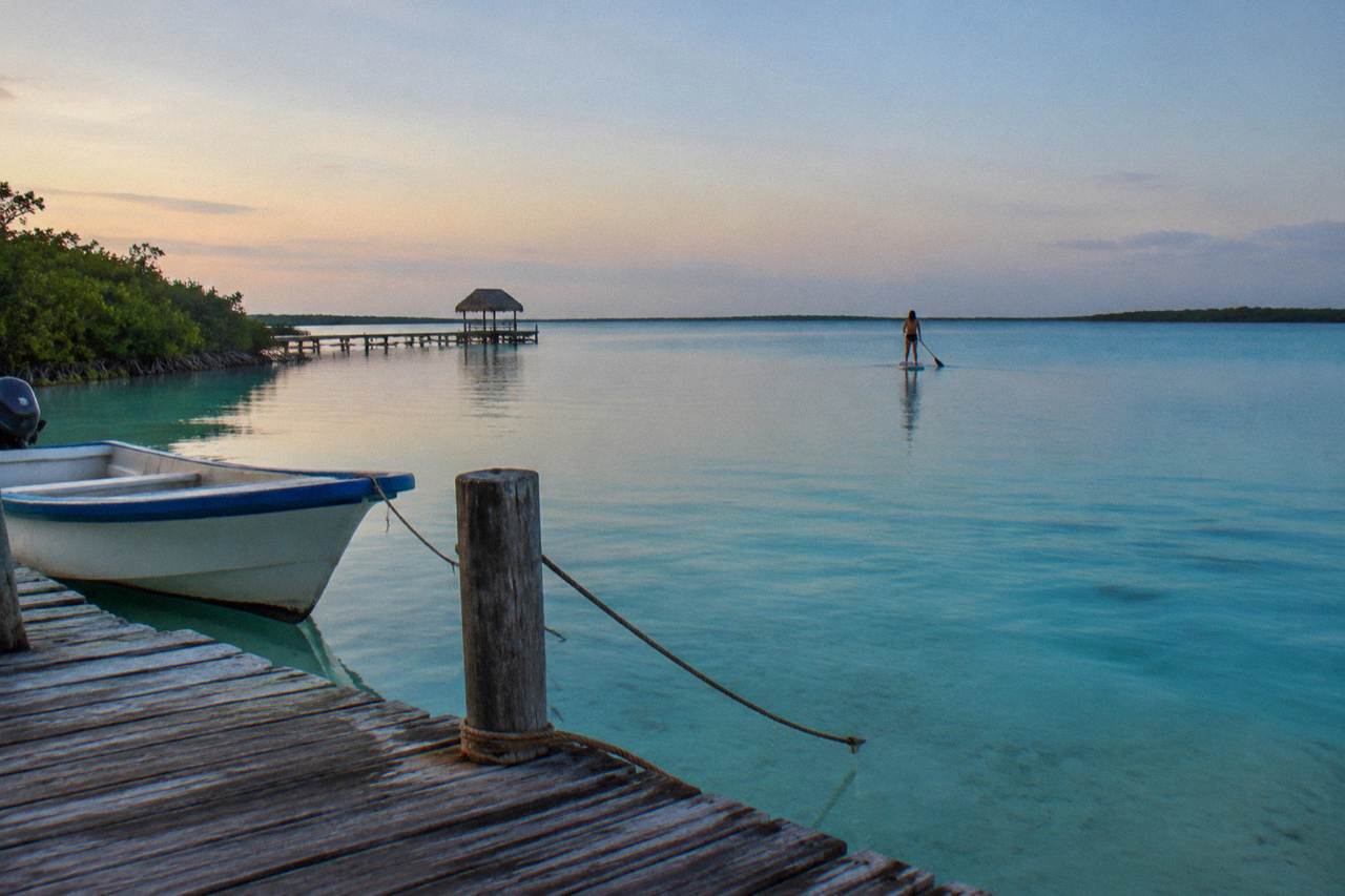 Calm turquoise water of Bacalar Lagoon at first light with a wooden dock in the foreground