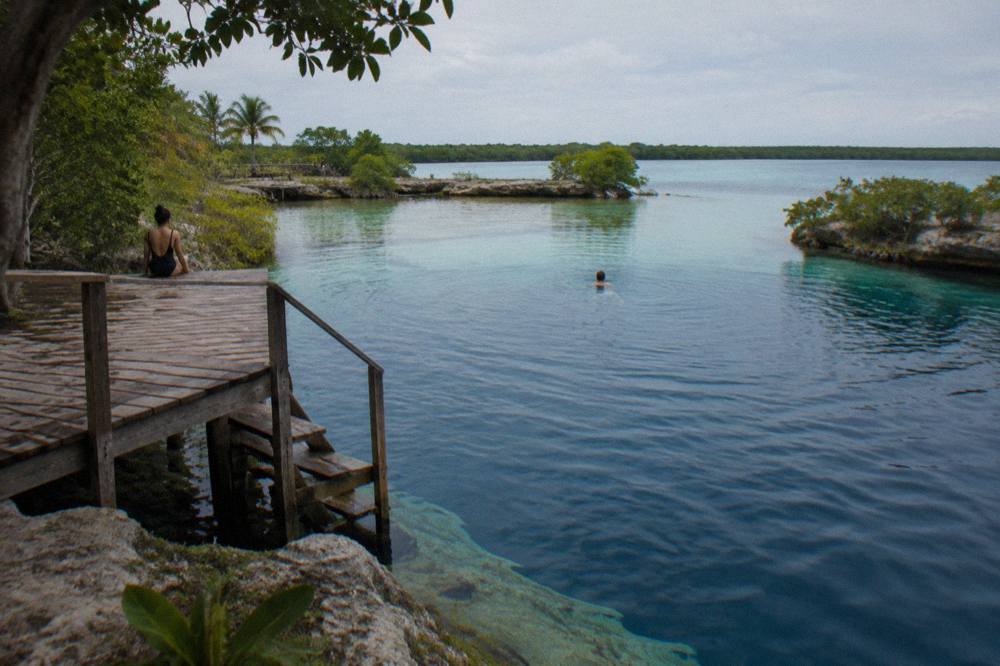 Wooden swim platform extending over deep blue cenote water surrounded by trees