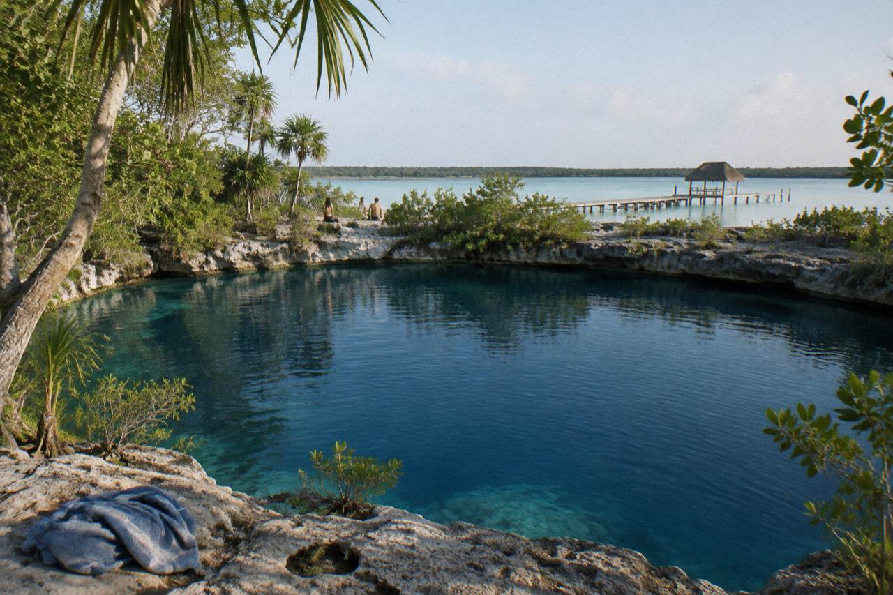 Clear blue water of Cenote Azul seen from its rocky edge with green trees