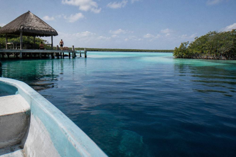 A small boat floating over dark deep water in the middle of a bright turquoise lagoon