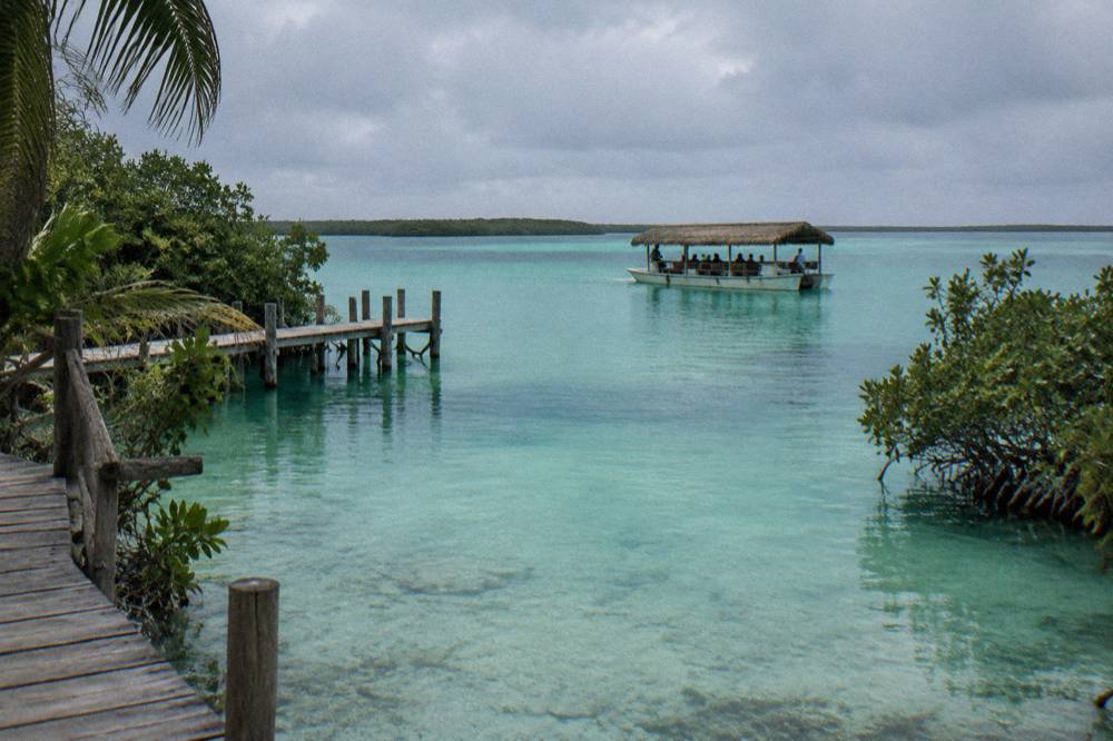 A tour boat with passengers drifting over an emerald green patch of lagoon water