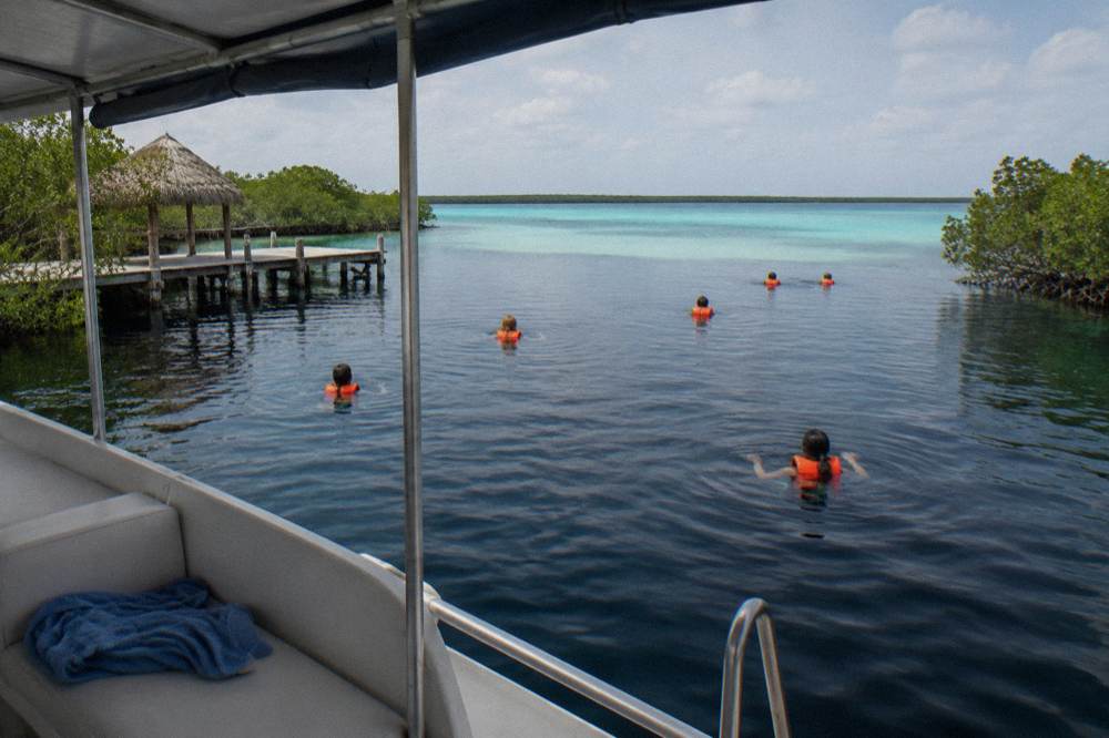 Swimmers in life vests floating in deep dark water beside a boat in a turquoise lagoon