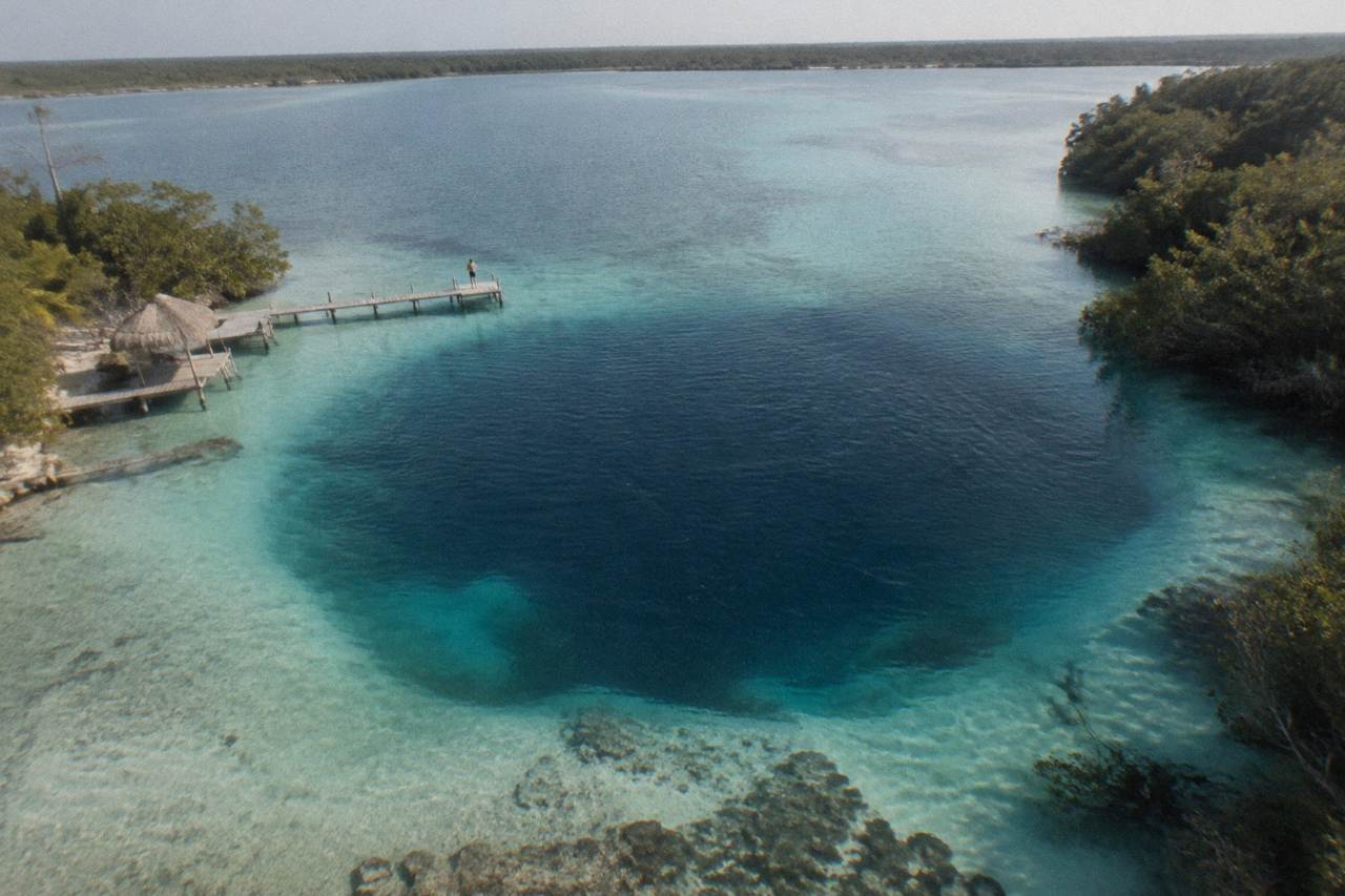 Deep blue and dark water circles inside a wide turquoise lagoon surrounded by mangroves