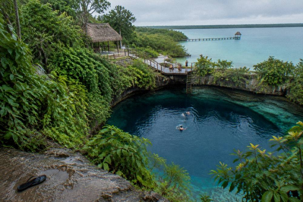 Steep green cliffs around a deep blue cenote pool in the Bacalar area