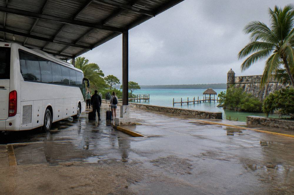 Intercity tour bus parked at a small terminal in a sunny Mexican town