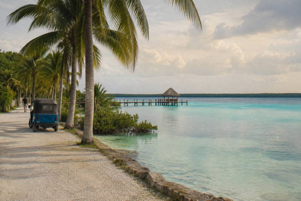 Quiet waterfront road with palm trees looking across calm turquoise lagoon water
