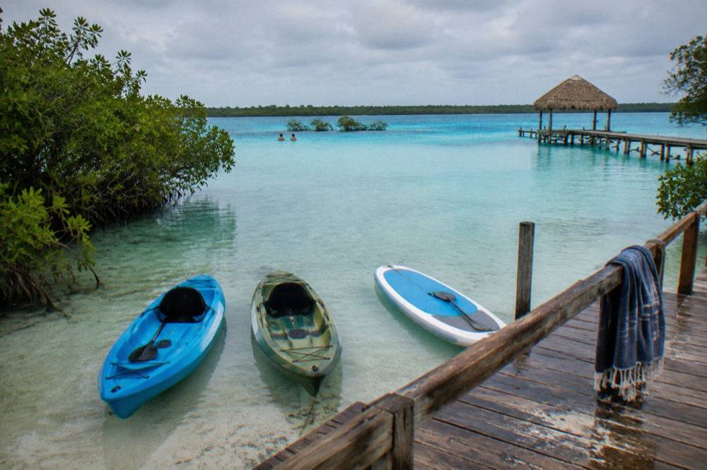 Kayaks and paddleboards resting in shallow turquoise water beside a wooden dock