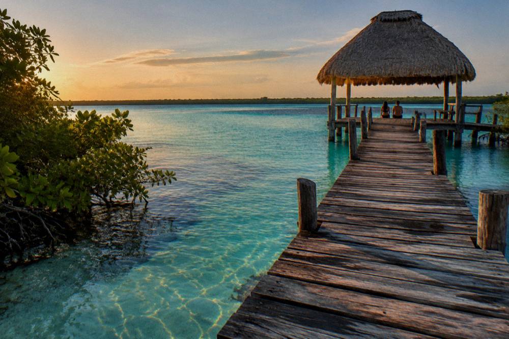 Wooden walkway and thatched shade palapa beside clear shallow channel water