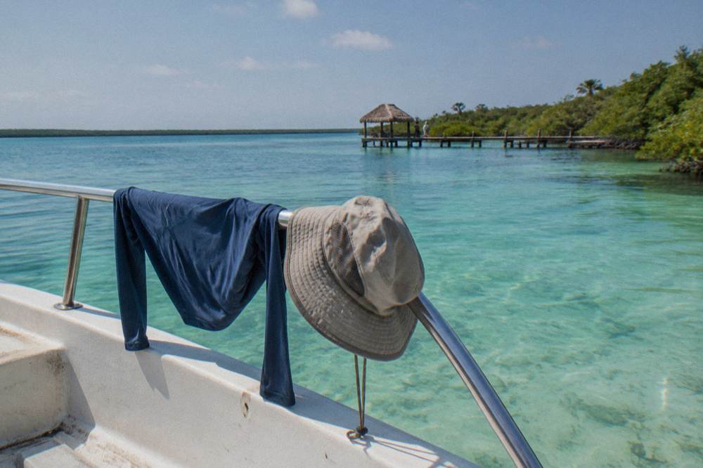 A long-sleeve rash guard and hat drying on a boat rail beside the lagoon